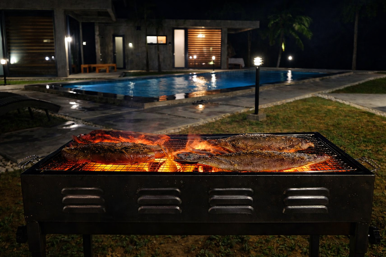 Fresh fish on a charcoal grill beside the lit pool at night