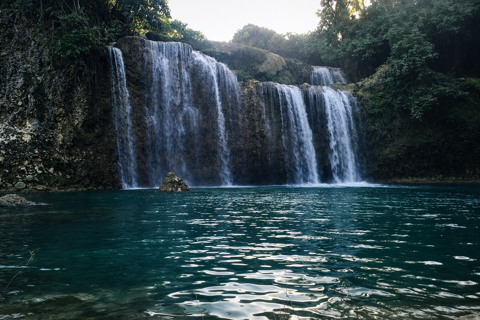 Bolinao Falls 1, the larger waterfall, dropping over a high cliff into a deep, dark basin.