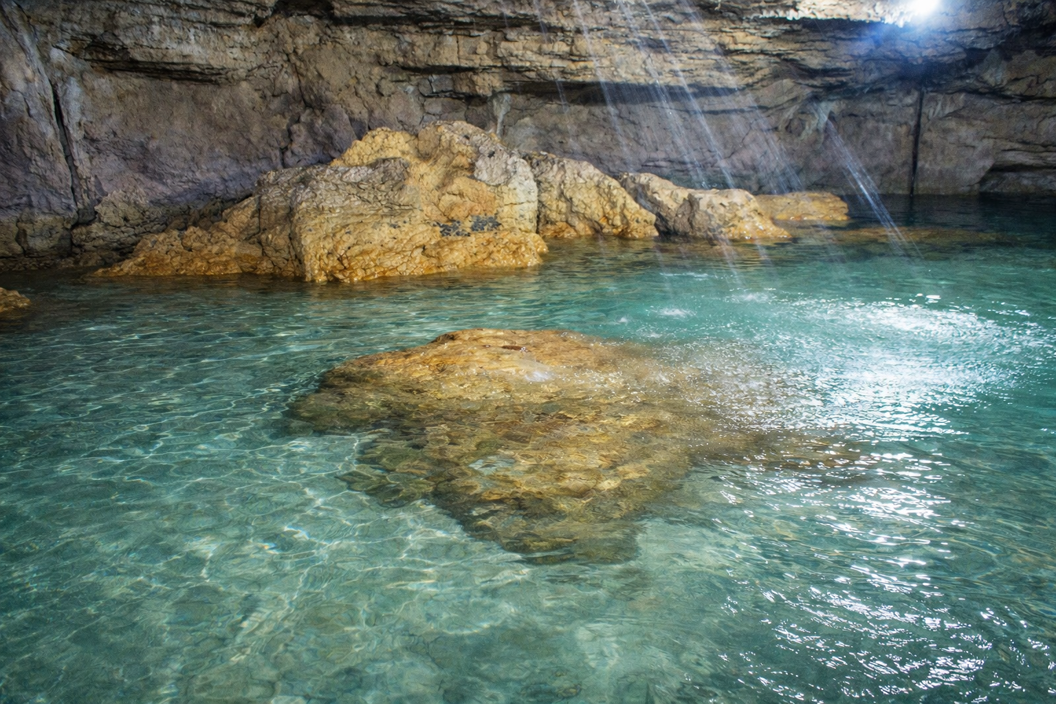 The mouth of one of the Bolinao caves, with shallow spring water lit by daylight filtering through the opening.